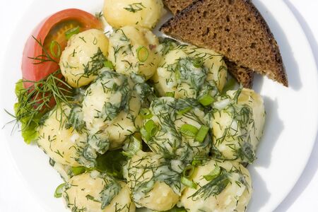 Boiled young potatoes and bread with herbs on plateの写真素材