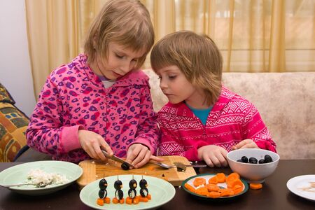 Children make canapes in the form of a penguin from olives, carrots and cottage cheeseの写真素材