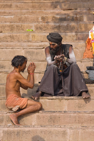 VARANASI, INDIA - DECEMBER 1: An unidentified sadhu and men sits on the ghat along the Ganges on December 1, 2012 in Varanasi, India. Tourism has drawn many alleged fake sadhus to Varanasiのeditorial素材