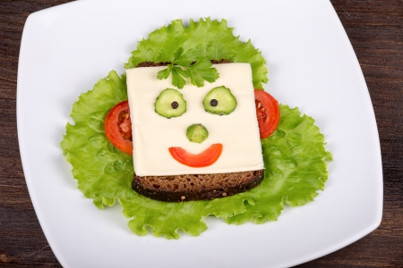 Fun food for kids - face on bread, made from cheese, lettuce, tomato, cucumber and pepper.の写真素材