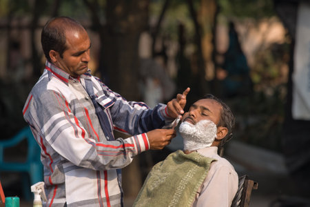 HARIDWAR, INDIA - NOVEMBER 8, 2012: An unidentified street barber shaving a man using an open razor blade on a bank of sacred river Ganges in Haridwar. Poor Indians flock to Haridwar for charity.のeditorial素材