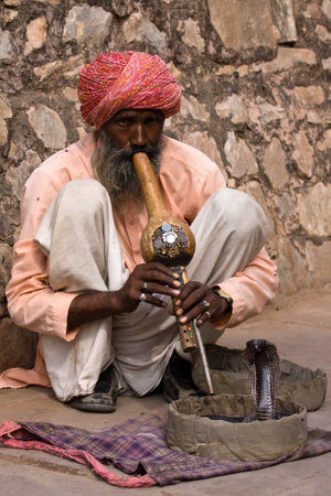 JAIPUR, INDIA - NOVEMBER 10, 2012: An unidentified snake charmer is playing the flute for the cobra sitting by the wall in the Fort Amber in Jaipur, Indiaのeditorial素材