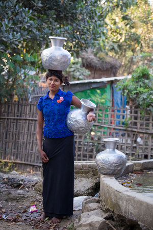 MRAUK-U, MYANMAR - JANUARY 27, 2016: Unidentified Burmese girl with big jugs with water. The local people are hospitable and friendly to touristsのeditorial素材
