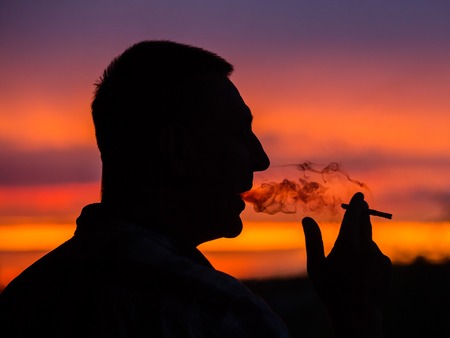 Silhouette of a man who smokes a cigarette on a sunset background, close upの写真素材