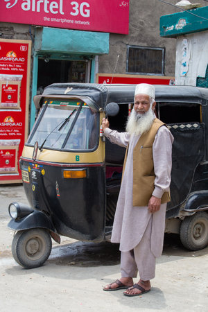 SRINAGAR, INDIA - JULE 11, 2015: Auto rickshaw taxis and muslim man on a road in Kashmir, India. These iconic taxis have recently been fitted with CNG powered engines in an effort to reduce pollutionのeditorial素材