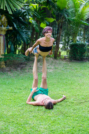 KOH PHANGAN, THAILAND - NOVEMBER 13, 2016 : Strong young couple doing acro yoga on green grass outdoors. Man and woman in park practising pair yoga poses.のeditorial素材