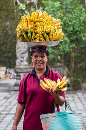BALI, INDONESIA - APRIL 14, 2017 : Portrait of an unidentified woman together with bananas on her head on the market by the water temple Tirta Empul.のeditorial素材