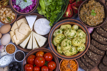 Assorted food on wooden background. Boiled young potatoes, beans, braised cabbage, beet salad with cottage cheese, sliced cheeses, pickled tomatoes, korean carrot, black bread with seeds, green lettuce leaves, spice. Bowls and plates with ukrainian foodの写真素材