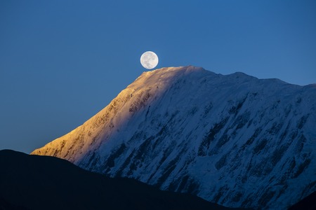 Beautiful landscape in Himalayas, Annapurna region, Nepal. Full moon during a sunrise on the background of snow-capped mountainsの写真素材