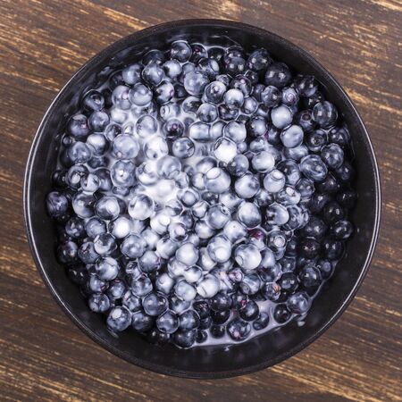 Fresh, ripe forest blueberries with sour cream in black plate. Close upの写真素材