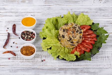 Rice with mushrooms, red tomato, onion, carrot and green lettuce leaves on rustic table background, close upの写真素材
