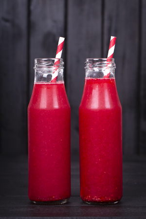Healthy eating, food, dieting and vegetarian concept - red raspberries juice in two glass bottle on black wooden background, close upの写真素材