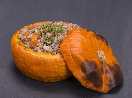 Tasty autumn stuffed pumpkin with buckwheat, carrot, onion, garlic and prunes on the background of black slate , close upの写真素材