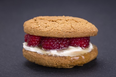 Healthy eating, food, dieting - oat cookies with raw raspberry, honey and soft cheese on the background of black slate , close upの写真素材