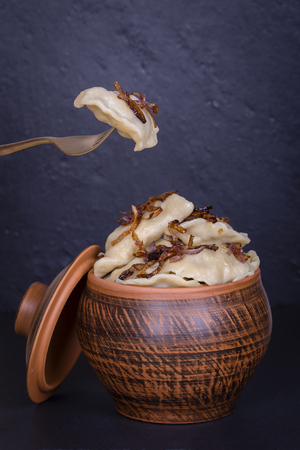 Ukrainian and Russian dishes - vareniki or dumplings with mashed potatoes or cottage cheese in clay pot on a black slate background, close upの写真素材