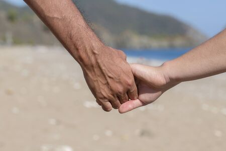 Couple hands held together on a natural sea background, close up