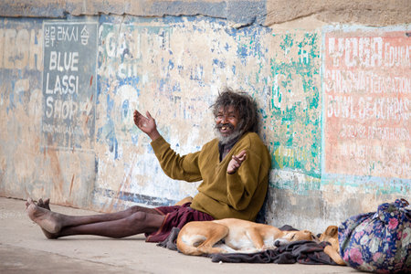 VARANASI, INDIA - JANUARY 26, 2017 : Poor man and dog on the ghats of the Ganges river in Varanasi, India . Close upのeditorial素材