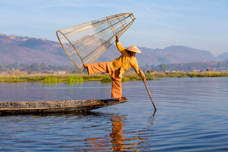 INLE LAKE, MYANMAR - JANUARY 14, 2016: Unidentified Burmese fisherman on bamboo boat catching fish in traditional way with handmade net. Inle lake, Myanmar, Burmaのeditorial素材