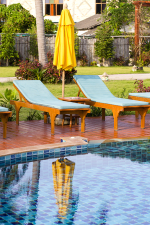 Chaise lounges and yellow umbrella next to the swimming pool in the morning, Thailandの写真素材