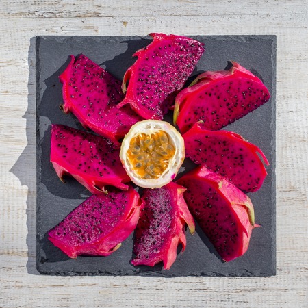 Exotic pink dragon fruit cut and passionfruit on background close up. Sweet tropical fruit, juicy pitaya and passion fruit cut on white wooden tableの写真素材