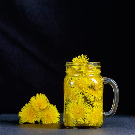 Dandelion yellow flower tea drink in glass mug on black background, close up. Concept of healthy eatingの写真素材