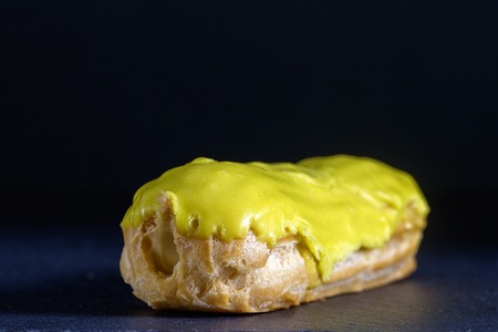 Pistachio eclair in glaze on black background, close up. Traditional French dessert