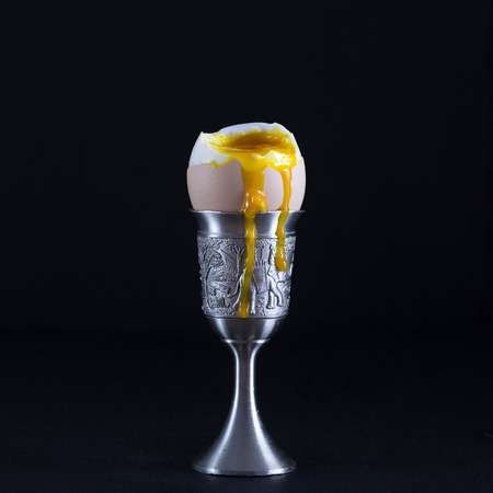 Soft boiled brown egg in eggcup on black background. Close up