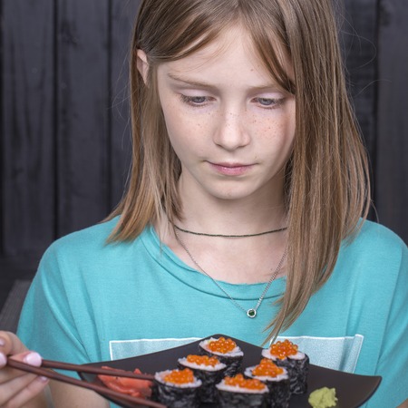 Pretty teen girl with sushi roll close up portrait, teenage girl eating japanese sushiの写真素材