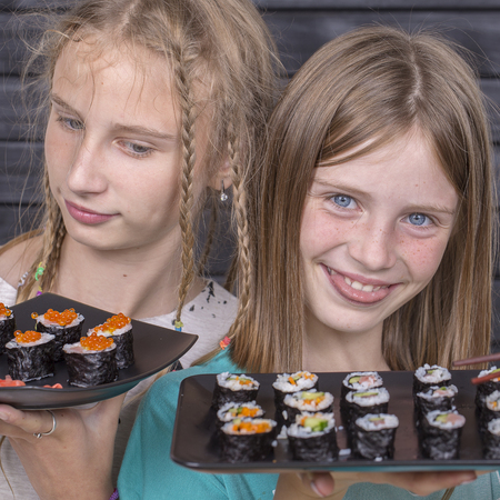 Two teen girl with sushi roll close up portrait, teenage girls eating japanese sushiの写真素材
