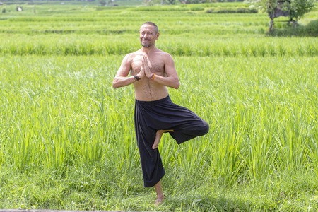 Man doing yoga and meditating in a position near a green rice terrace on the tropical island of Bali, Indonesia. Close upの写真素材