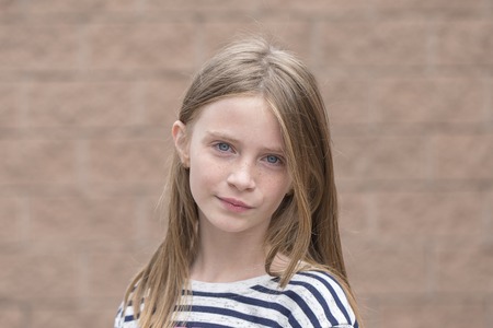 Beautiful blond young girl with freckles outdoors on wall background, close up portrait
