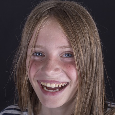 Beautiful blond young girl with freckles indoors on a black background, close up portrait