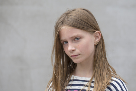 Beautiful blond young girl with freckles outdoors on wall background, close up portraitの写真素材