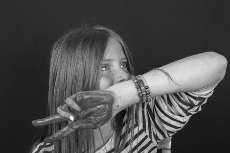 Beautiful blond young girl with freckles and hands painted in colorful paints indoors , close up portrait, black and whiteの写真素材