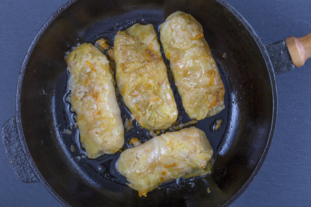 Ukrainian dishes - homemade stuffed cabbage rolls with rice and meat in tomato sauce in a frying pan on a black slate background, close up, top viewの写真素材