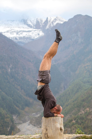 HIMALAYAS, ANNAPURNA REGION, NEPAL - OCTOBER 15, 2016 : Portrait man standing on her head doing yoga...