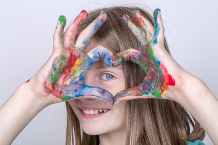 Portrait young girl and child hands painted make a heart shape, close up. Schoolgirl hands forming a colorful heart symbolの写真素材