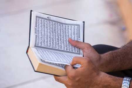 SHARM EL-SHEIKH, EGYPT - MAY 17, 2018: Egyptian man reading the book of Islam, al Quran is a holy book of Islamic religion, Al-Quran in hand - holy book of Muslims. Sharm El Sheikh, South Sinai, Egyptのeditorial素材