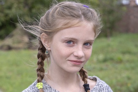 Beautiful blond young girl with freckles outdoors on nature background, close up portraitの写真素材