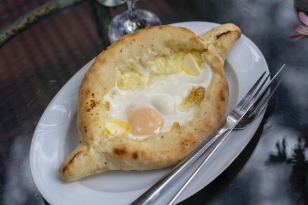 Adjarian khachapuri in restaurant. Open bread pie with cheese and egg yolk. Yummy georgian cuisine. Close upの写真素材