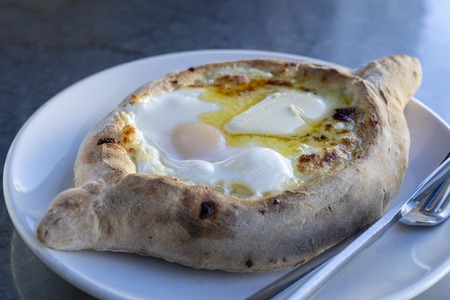 Adjarian khachapuri in restaurant. Open bread pie with cheese and egg yolk. Yummy georgian cuisine. Close upの写真素材