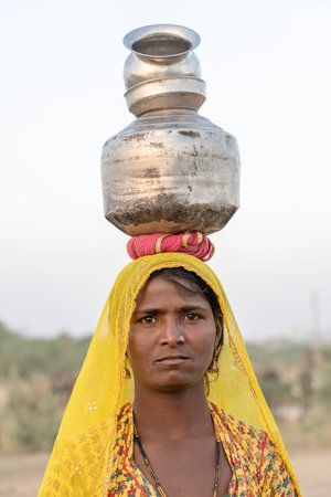 PUSHKAR, INDIA - NOVEMBER 13, 2018 : Indian poor woman with pots on her head on time Pushkar Camel...