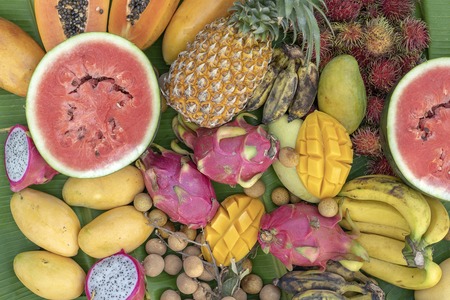 Tropical fruits assortment on a green banana leaves. Yummy dessert, close up. Mango, papaya, banana, pitahaya and watermelon, top viewの写真素材