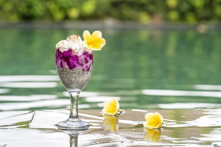 Chia seeds pudding with red dragon fruit and white yogurt in a glass for breakfast on the background of the swimming pool water, close up. The concept of healthy eating.の写真素材