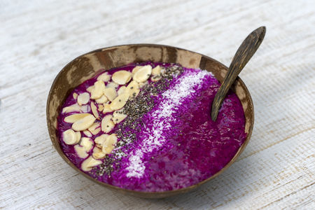 Red smoothie in coconut bowl with dragon fruit, avocado, almond flakes, coconut chips and chia seeds for breakfast , close up. The concept of healthy eating, superfood . Island Bali, Indonesiaの写真素材