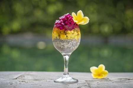 Chia seeds pudding with red dragon fruit, passion fruit, mango and avocado in a glass for breakfast on the background of the swimming pool water, close up. The concept of healthy eating.の写真素材