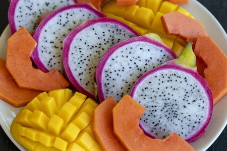 Tropical fruits assortment on a plate, close up. Many colorful ripe tropical fruits background. Mango, papaya and pitahayaの写真素材