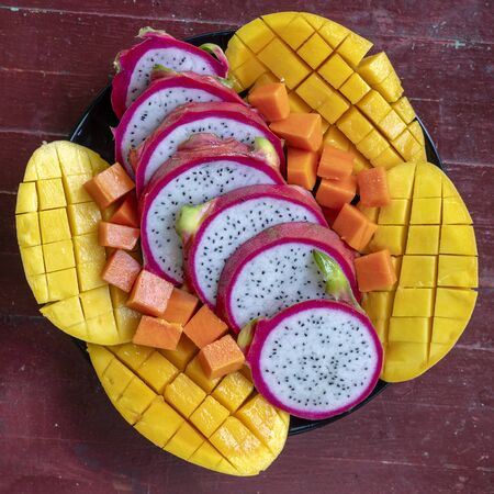 Tropical fruits assortment on a plate, close up. Many colorful ripe tropical fruits background. Mango, papaya and pitahayaの写真素材