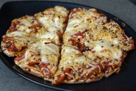 Homemade pizza ready to eat on a black plate, close up