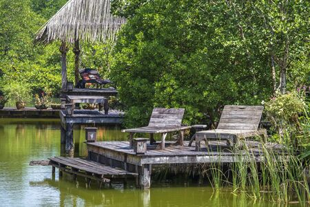 Two old wooden deck chairs near the lake water in a tropical garden, asia, Thailand. Travel and nature conceptの写真素材